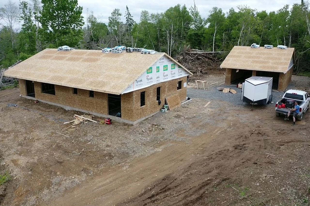 Aerial view of a bungalow and matching detached garage, both framed and sheathed, on a cleared lot.