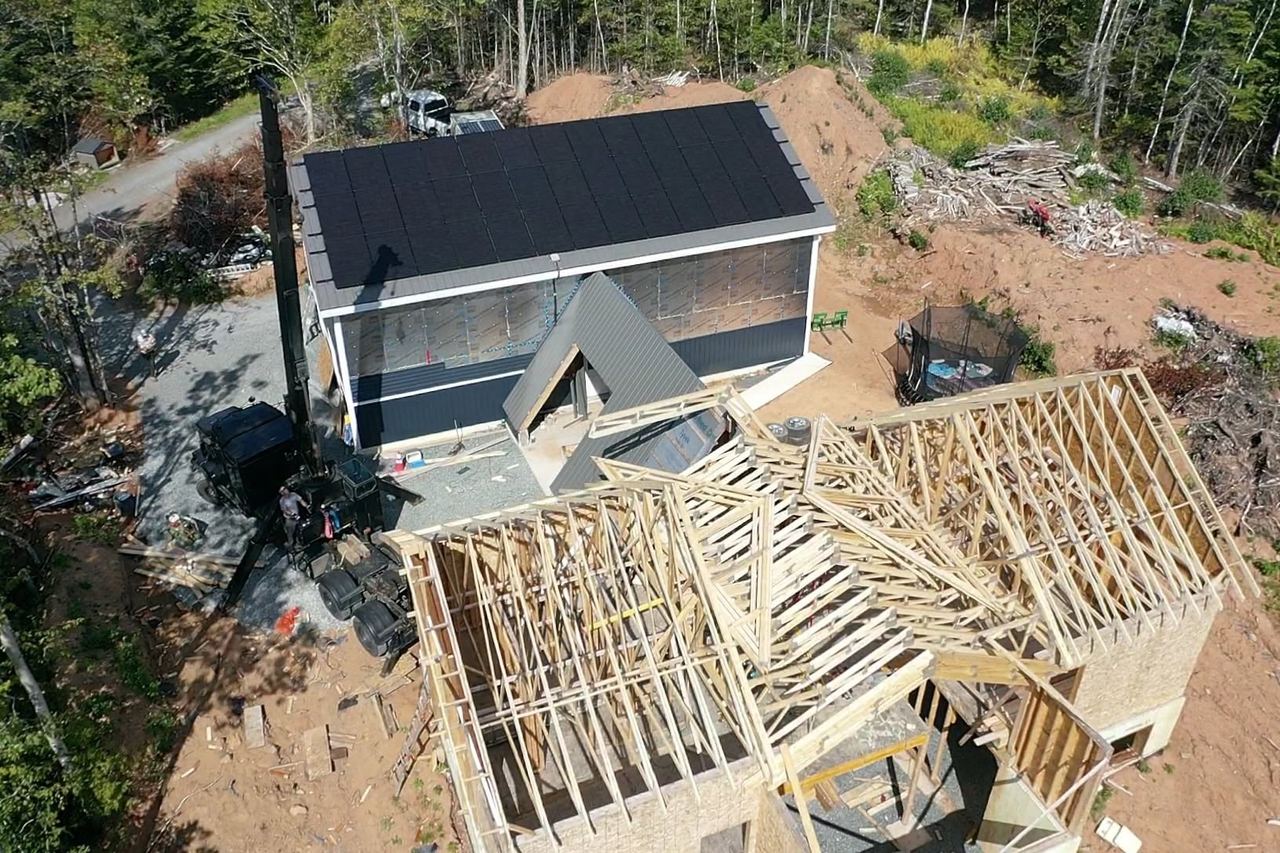 Aerial view of a Nova Scotia house under construction, with a crane setting roof trusses onto the framed walls.