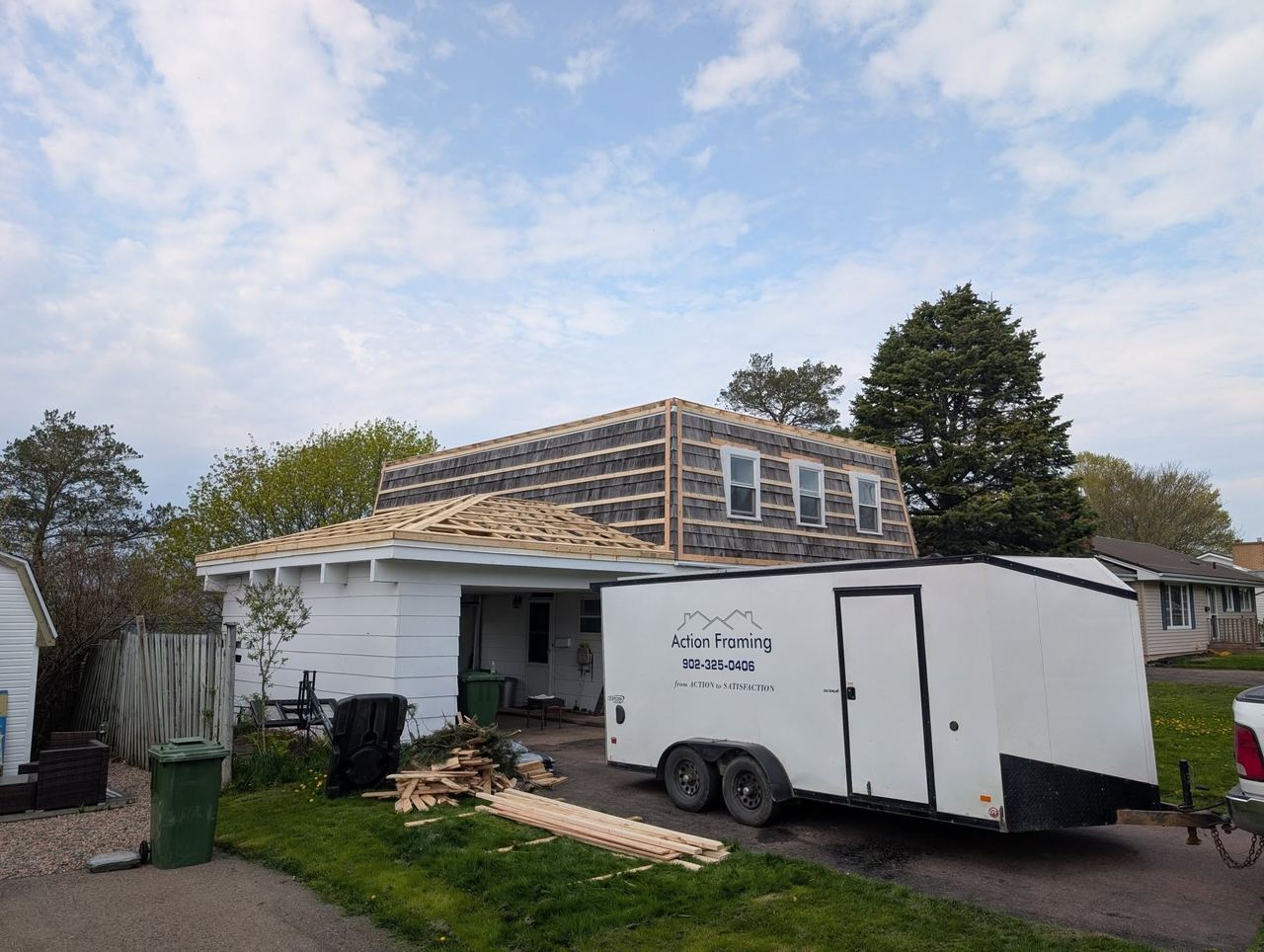 Dormer being framed into the roof of an existing white house, with the Action Framing trailer parked in the driveway.