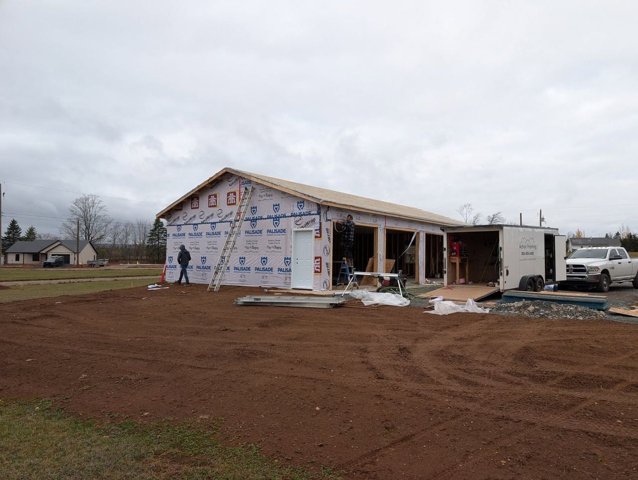Garage shell wrapped in housewrap with a crew member and the work trailer on site.