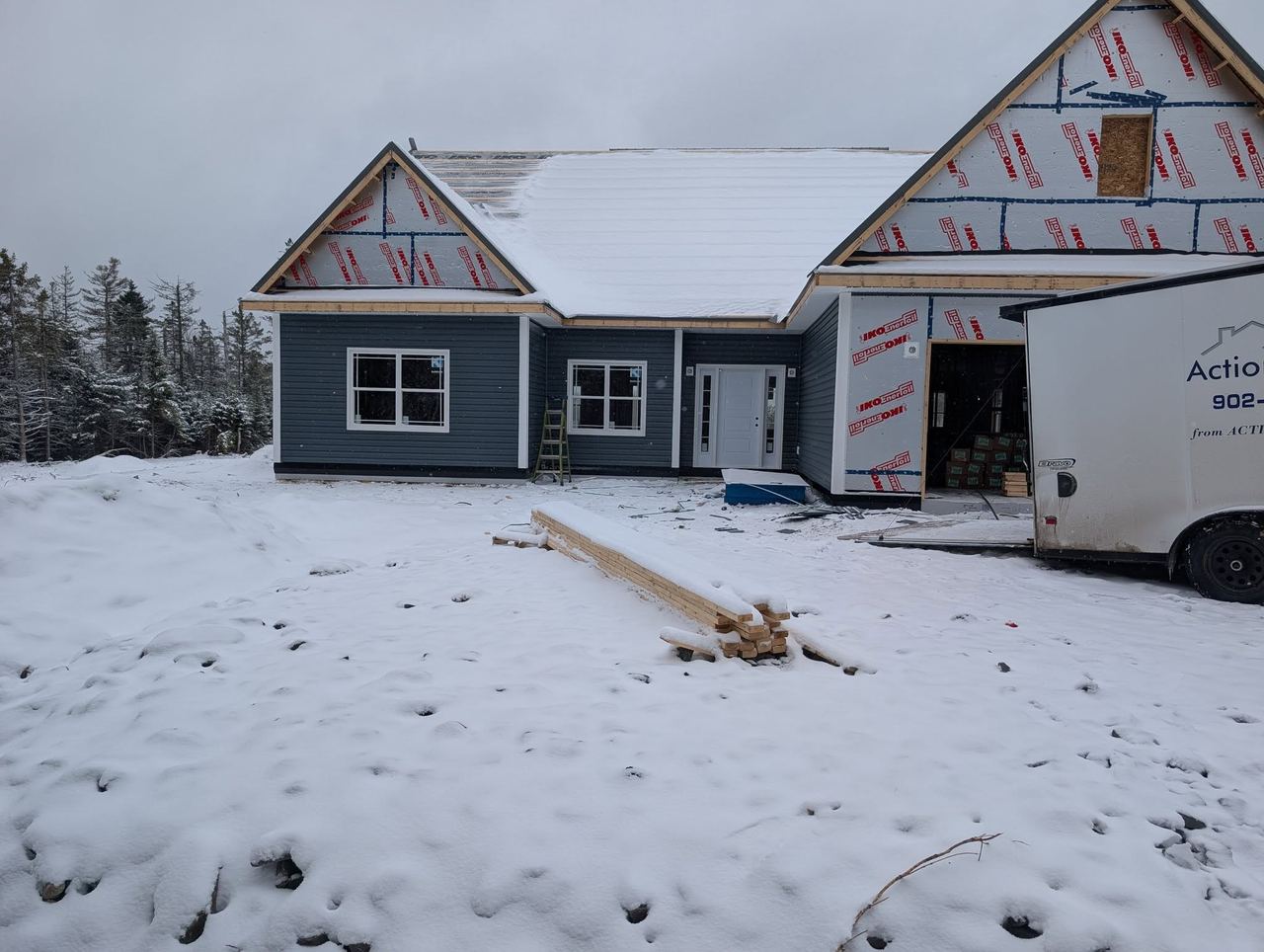 Blue-sided house dried in during winter with the Action Framing trailer parked at the garage door.