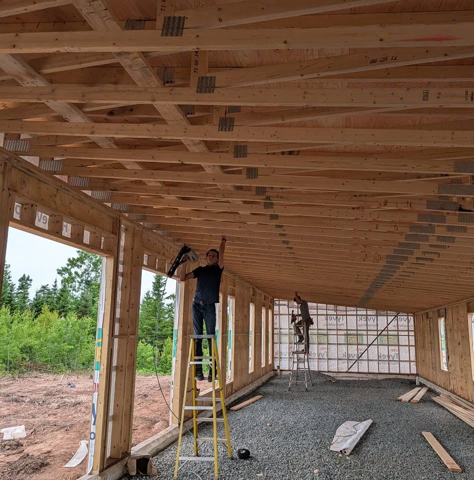 Interior framing with ceiling joists overhead and a carpenter working from a ladder.