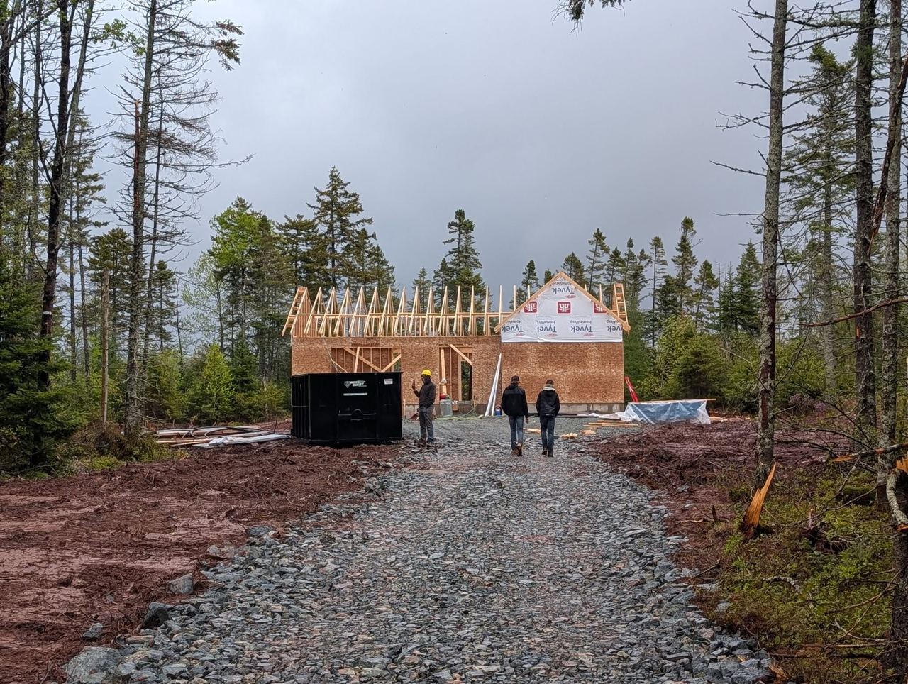Framed two-storey shell on a wooded Nova Scotia lot at the end of a fresh gravel driveway.