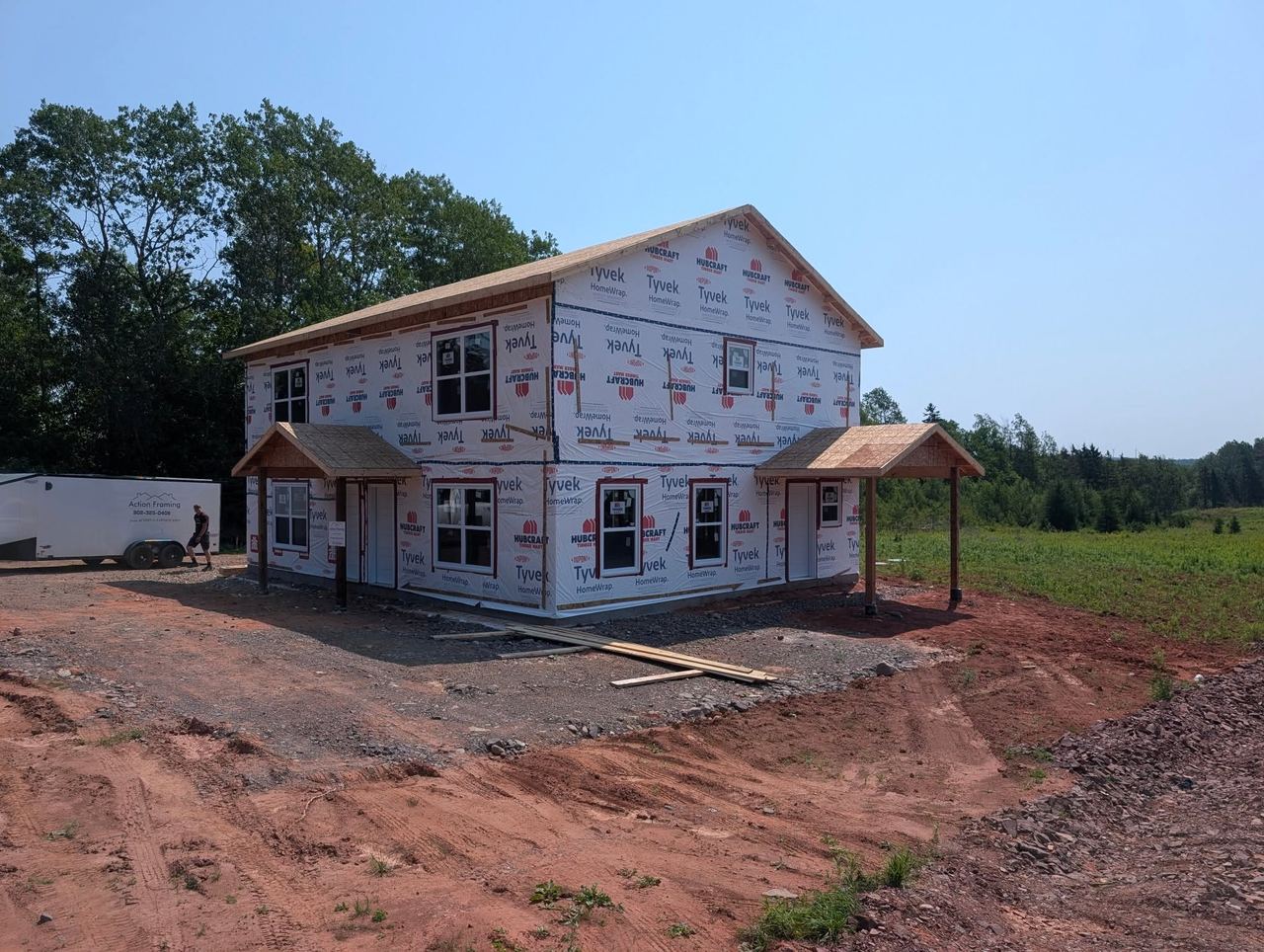 Two-storey house framed and wrapped in Tyvek with covered porch overhangs, on a clear day in central Nova Scotia.