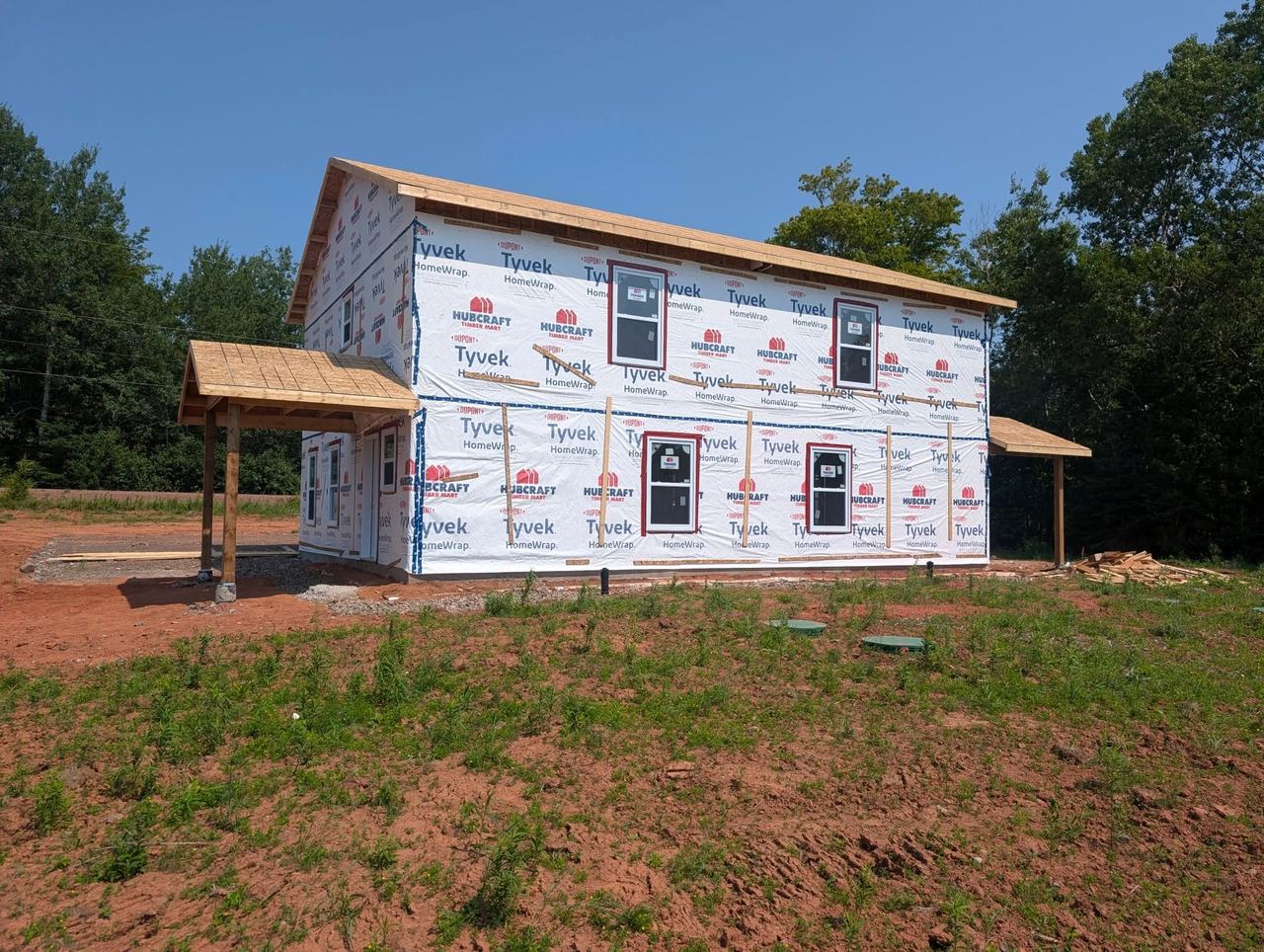 Two-storey home framed, sheathed and wrapped, with covered porch roofs framed at both ends.